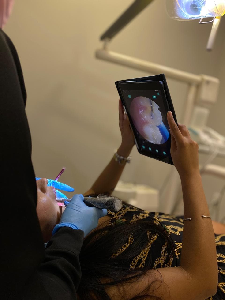 Paciente deitada na cadeira segurando um tablet que mostra, ampliado e ao vivo, o próprio dente sendo examinado pela câmera intraoral