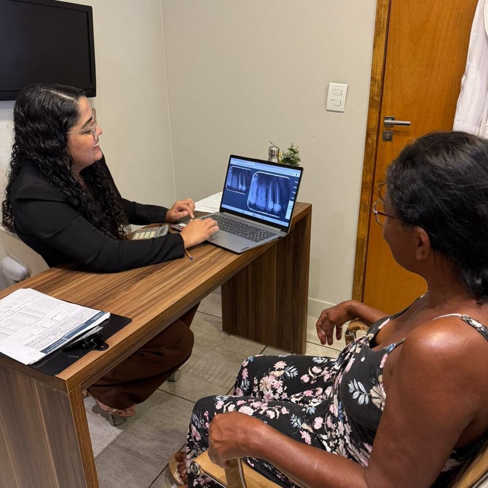 Dentista mostrando as radiografias na tela do computador para a paciente sentada à mesa, durante o planejamento do tratamento